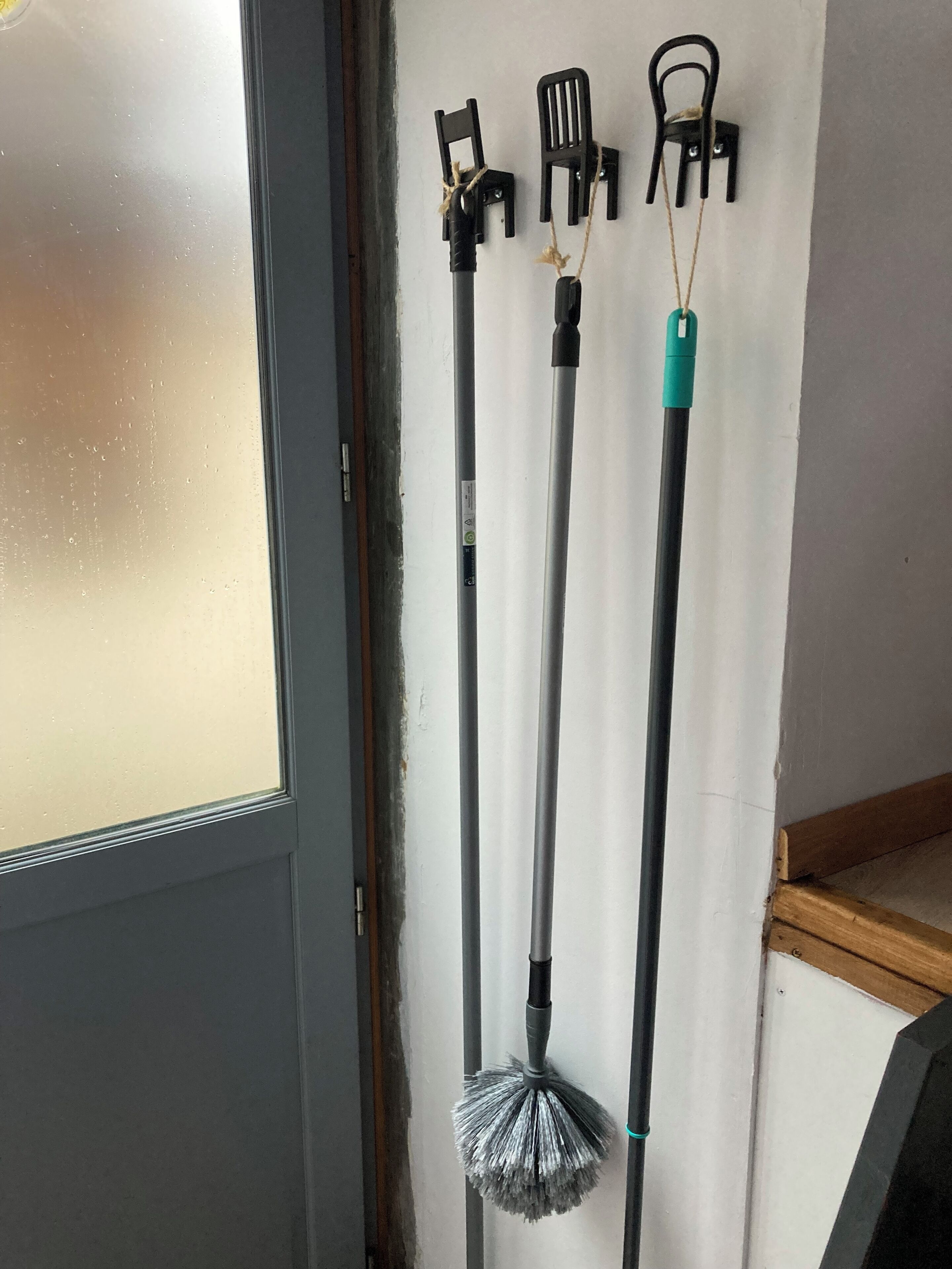 A room with a door, a window with condensation, and three cleaning tools hanging on the wall.