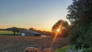 Une enseigne en bois portant l’inscription « GÎTES CHEZ CLAUDIA », située dans un cadre rural, avec un coucher de soleil en arrière-plan.