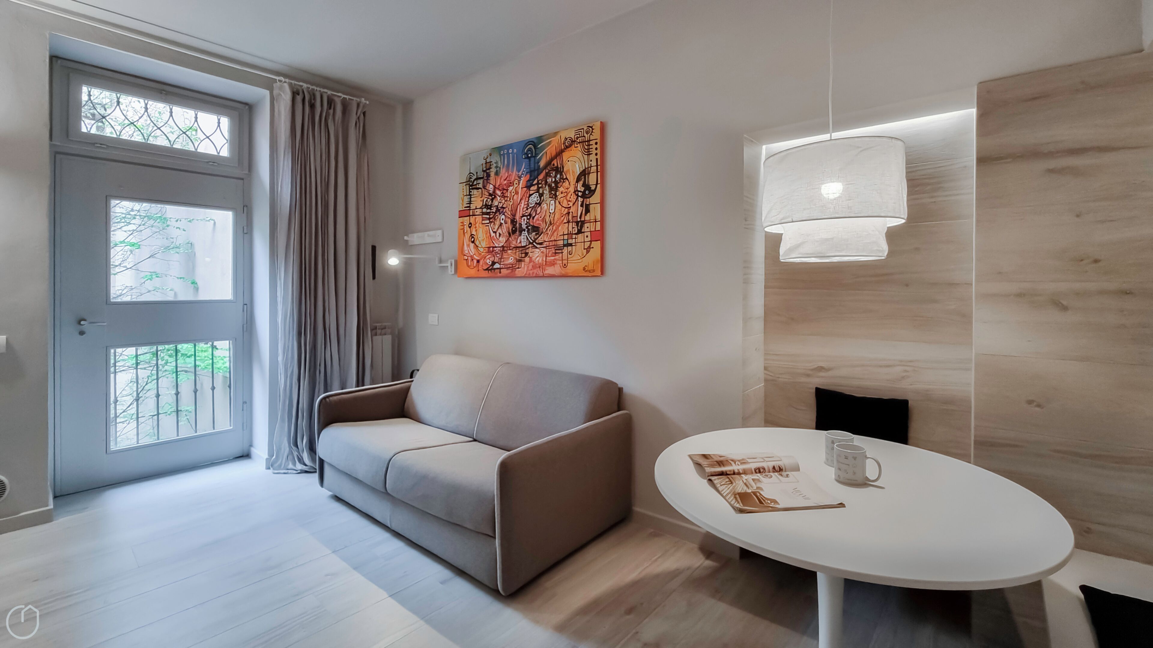 A modern living room with a sofa, a round table, and a painting on the wall.