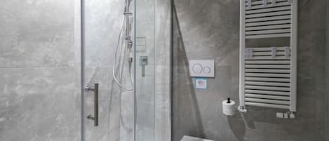 A modern bathroom with a glass shower enclosure, a towel rack, and a toilet paper holder.