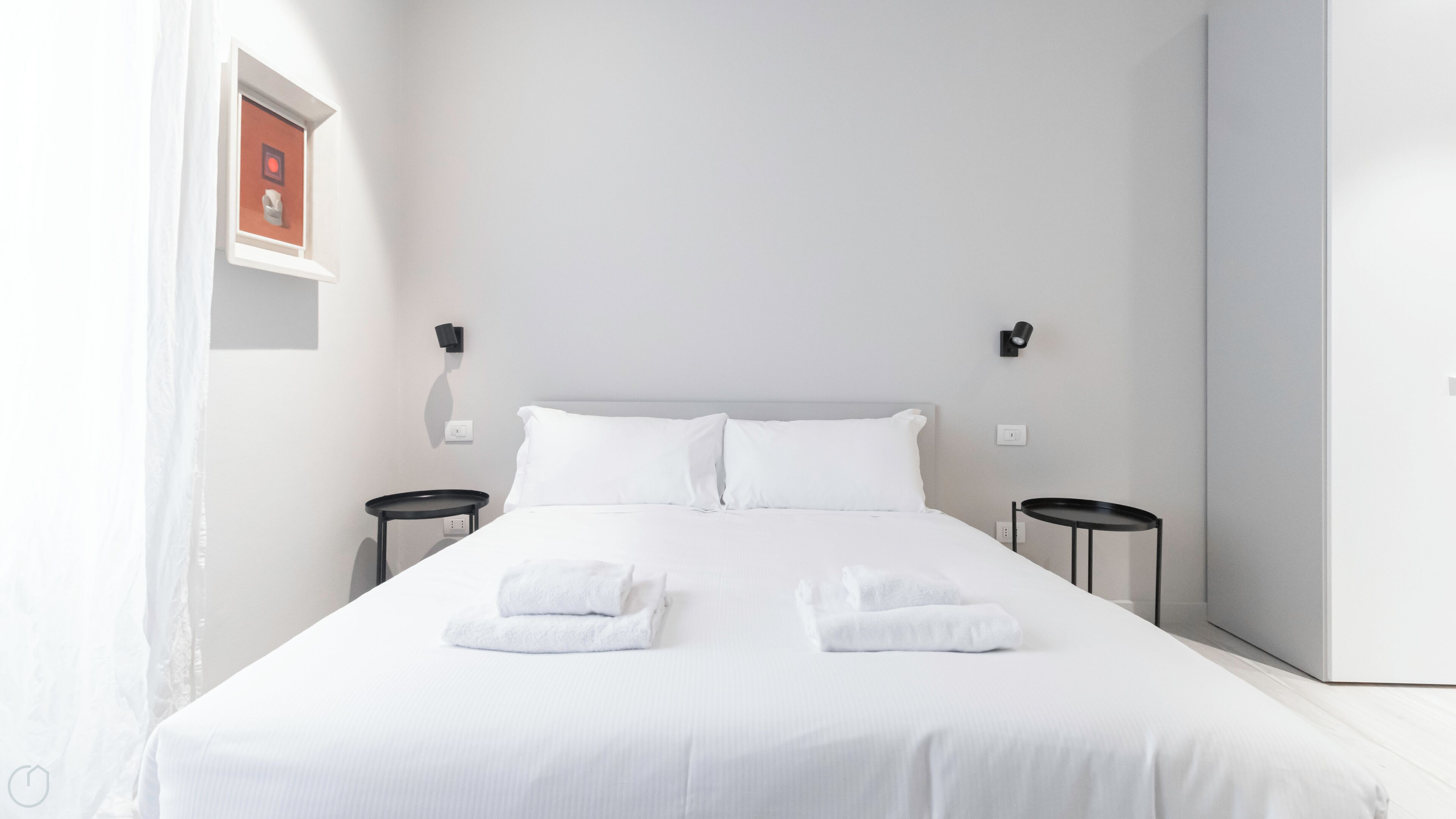 A neatly made bed with white linens and towels, two bedside tables, and a framed picture on the wall.