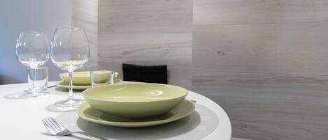 A dining table set with a green bowl, two wine glasses, a fork, and a small candle holder.