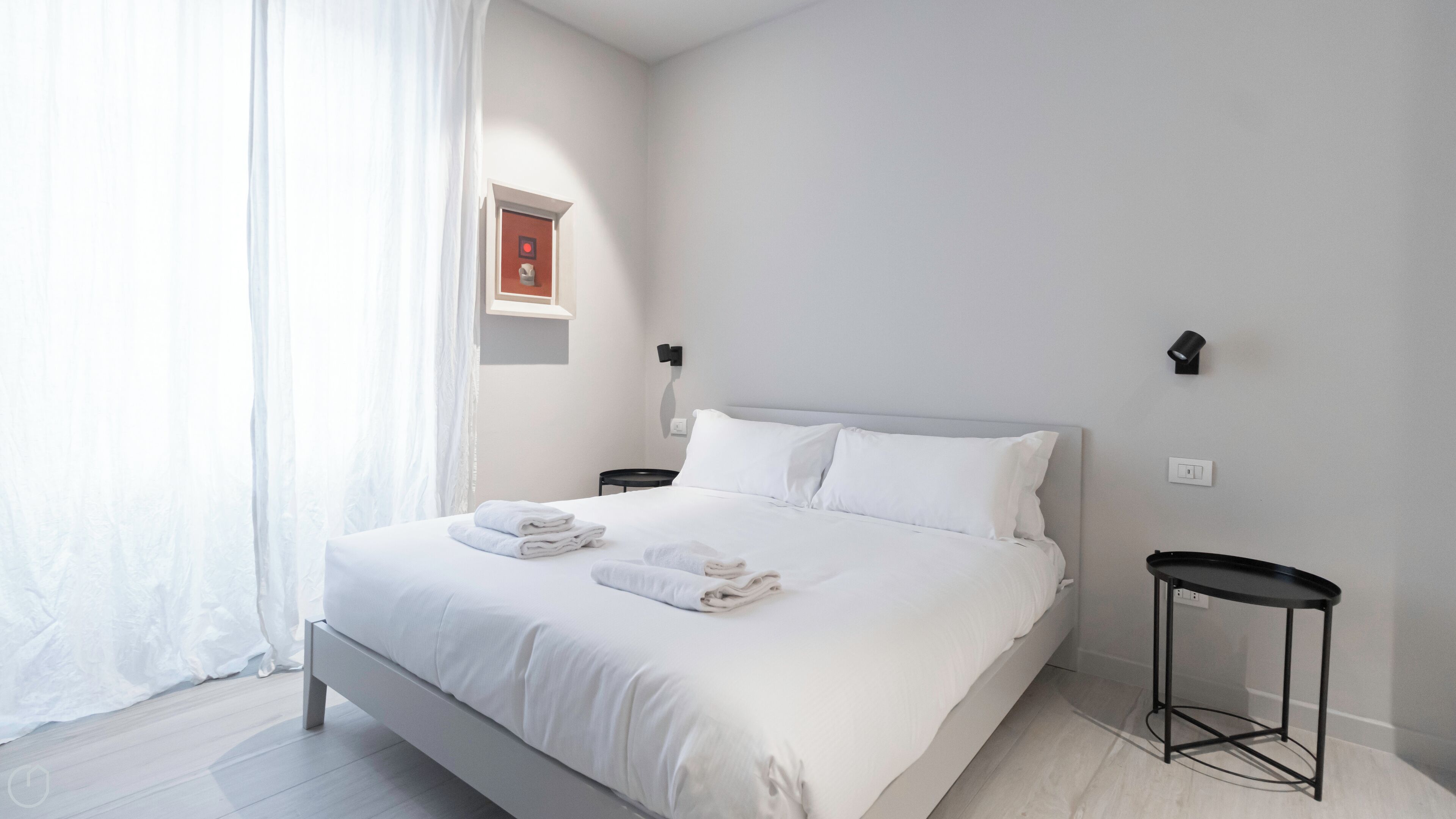 Habitació d'hotel moderna amb un llit gran, roba de llit blanca, una tauleta de nit i una taula petita.