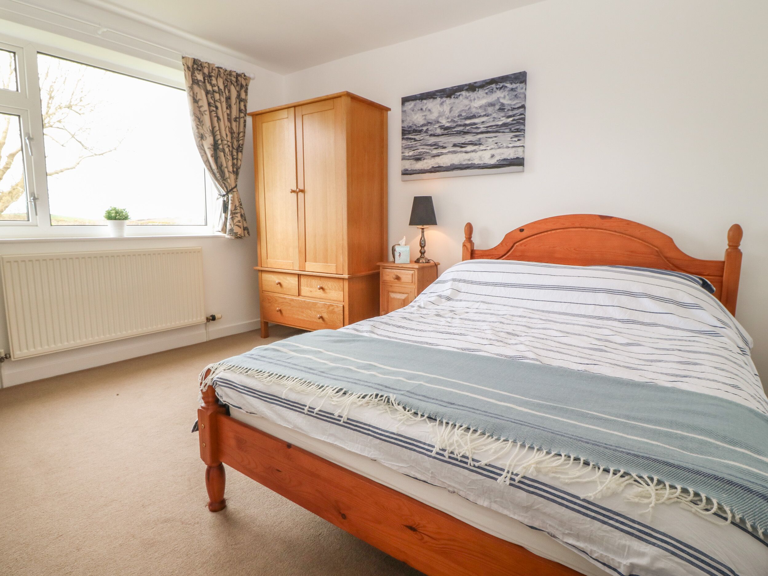 A bedroom with a wooden bed, a nightstand, a wardrobe, a radiator, and a window with curtains.