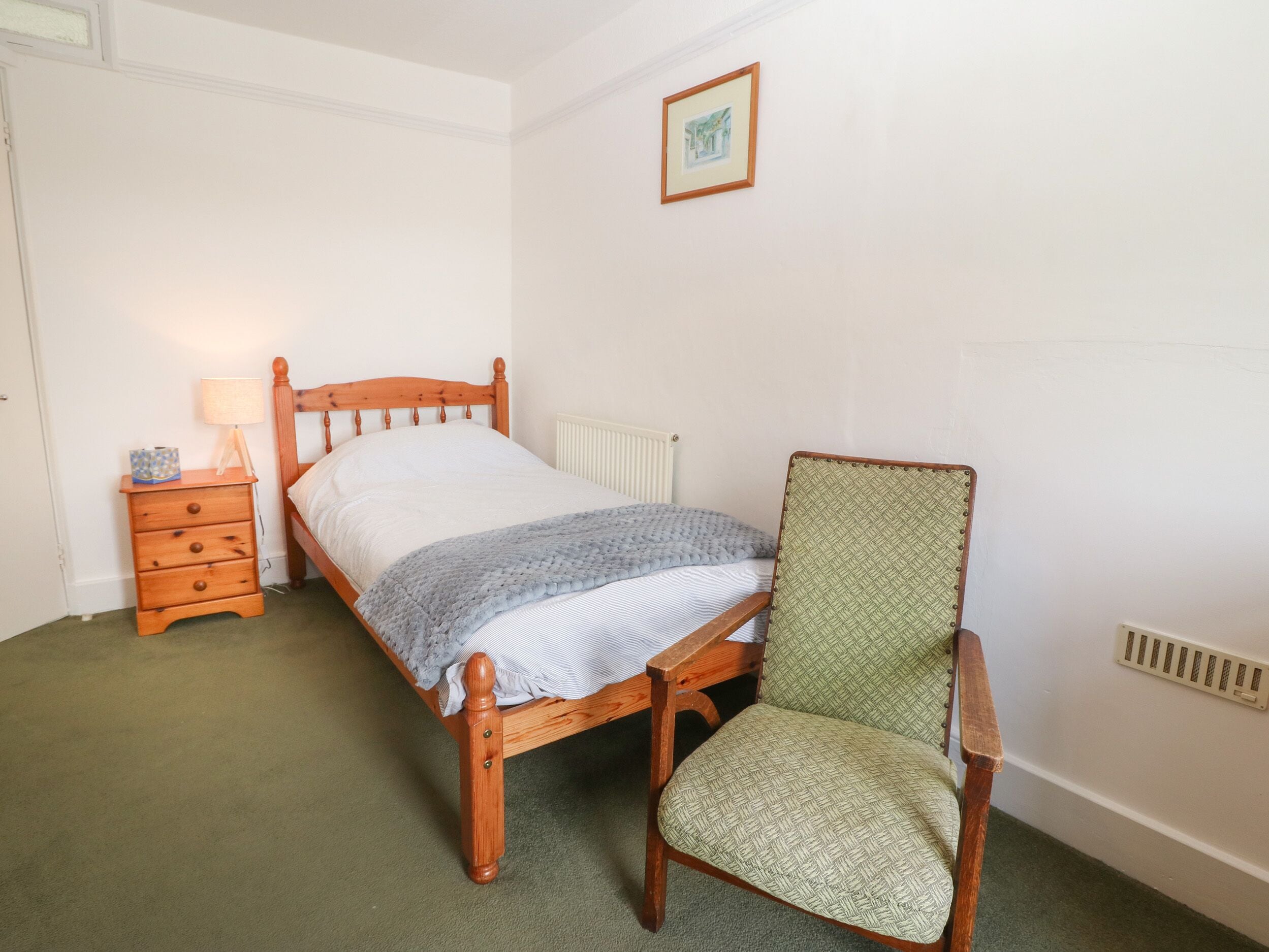 A bedroom with a wooden bed, a nightstand, a chair, and a framed picture on the wall.