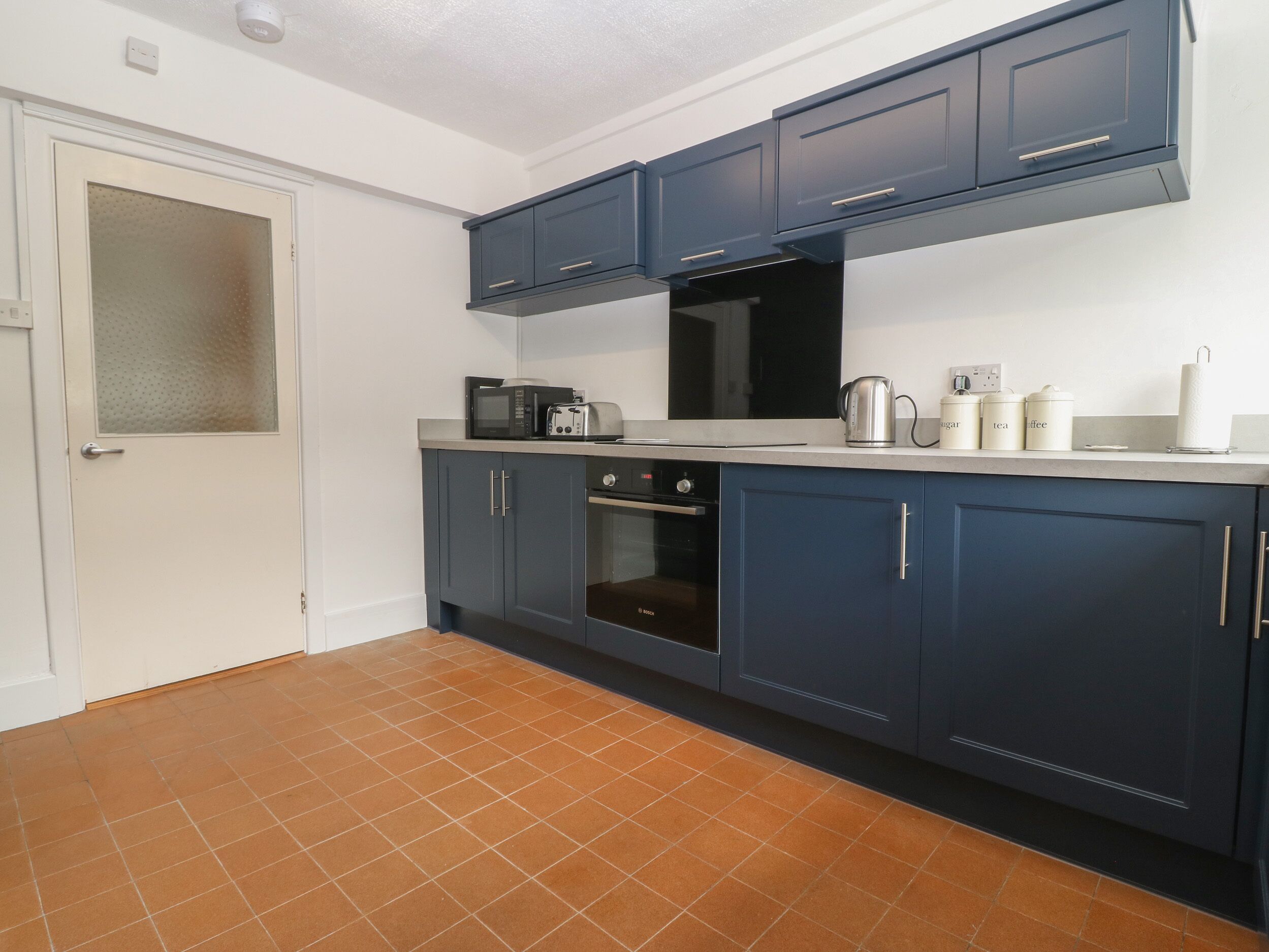 A kitchen with dark blue cabinets, a microwave, toaster, kettle, and coffee maker on the countertop.