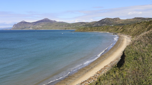 A coastal landscape with a sandy beach, clear blue sea, and distant mountains. - Dolafon (Pwllheli)