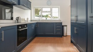 A modern kitchen with dark blue cabinets, a stainless steel kettle, and a visible trash bin. - Dolafon (Pwllheli)
