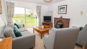 A living room with a sofa set, a television, a fireplace, and a view of the outdoors. - Dolafon (Pwllheli)