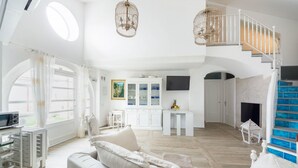 A spacious living area with a white sofa, a dining table, and a staircase with blue steps. - Luxury Villa Vittoria- Villa With Garden Swimming Pool and Jacuzzi Overlooking the sea (Maiori)