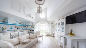 A modern kitchen with white cabinetry, a dining area with a white table, and a sofa. - Luxury Villa Vittoria- Villa With Garden Swimming Pool and Jacuzzi Overlooking the sea (Maiori)