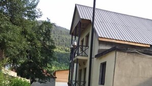 Un edificio con entrada empedrada, balcón y montañas al fondo.