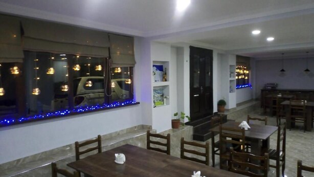 Un comedor con mesas y sillas de madera, un ventanal con luces azules y una zona de cocina al fondo.
