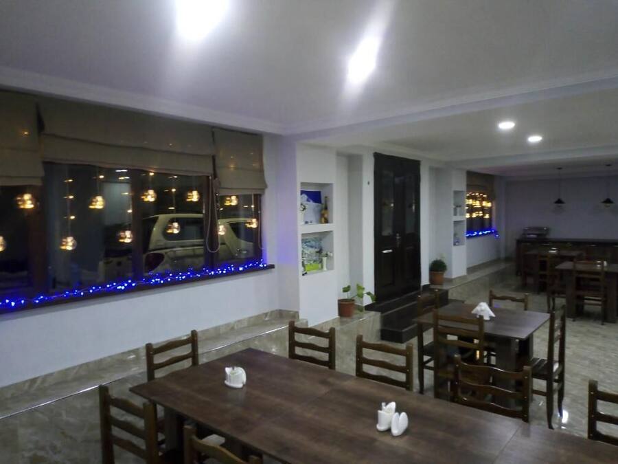 Un comedor con mesas y sillas de madera, un ventanal con luces azules y una zona de cocina al fondo.