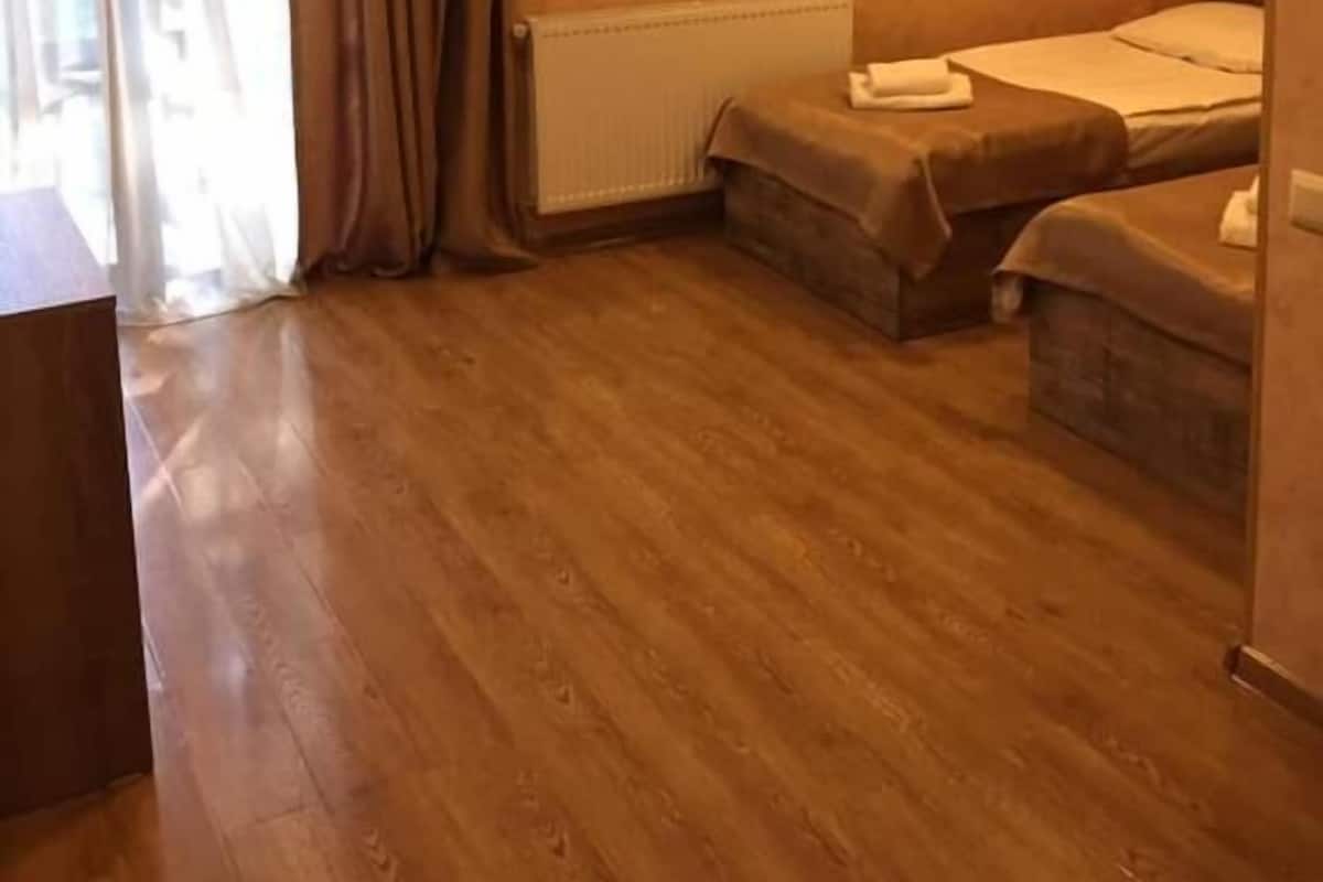 A room with two single beds, a radiator, wooden flooring, and a window with curtains.