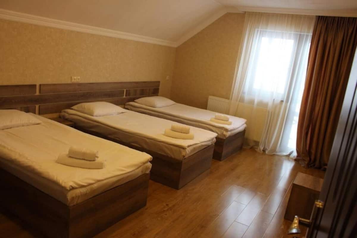 A hotel room with three single beds, wooden headboards, and a window with curtains.