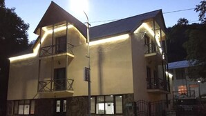 Un edificio de dos pisos con un balcón en el segundo nivel, fachada de piedra y entrada protegida por una reja.