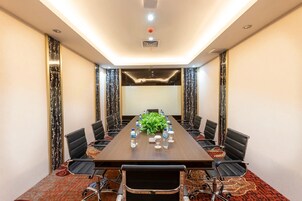 Un salón de conferencias con una larga mesa, sillas, botellas de agua y una planta.