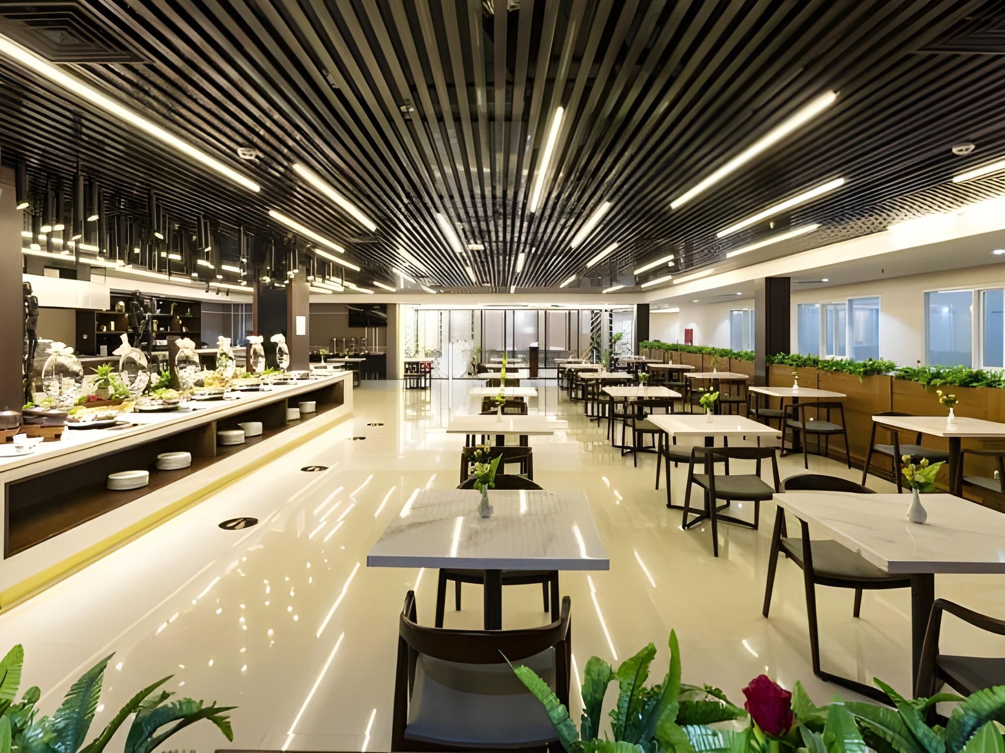 Una cafetería moderna con mesas y sillas largas, piso pulido e iluminación lineal en el techo.