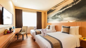 Une chambre d’hôtel avec deux lits, un bureau avec une chaise, une télévision et un tableau représentant un paysage.