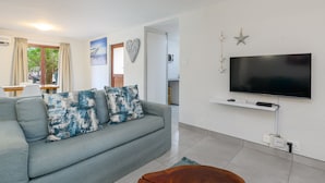 A modern living room with a grey sofa, a flat-screen TV mounted on the wall, and a wooden coffee table.