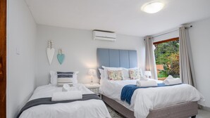 A hotel room with two beds, a window with curtains, an air conditioning unit, and a wall-mounted decorative piece.