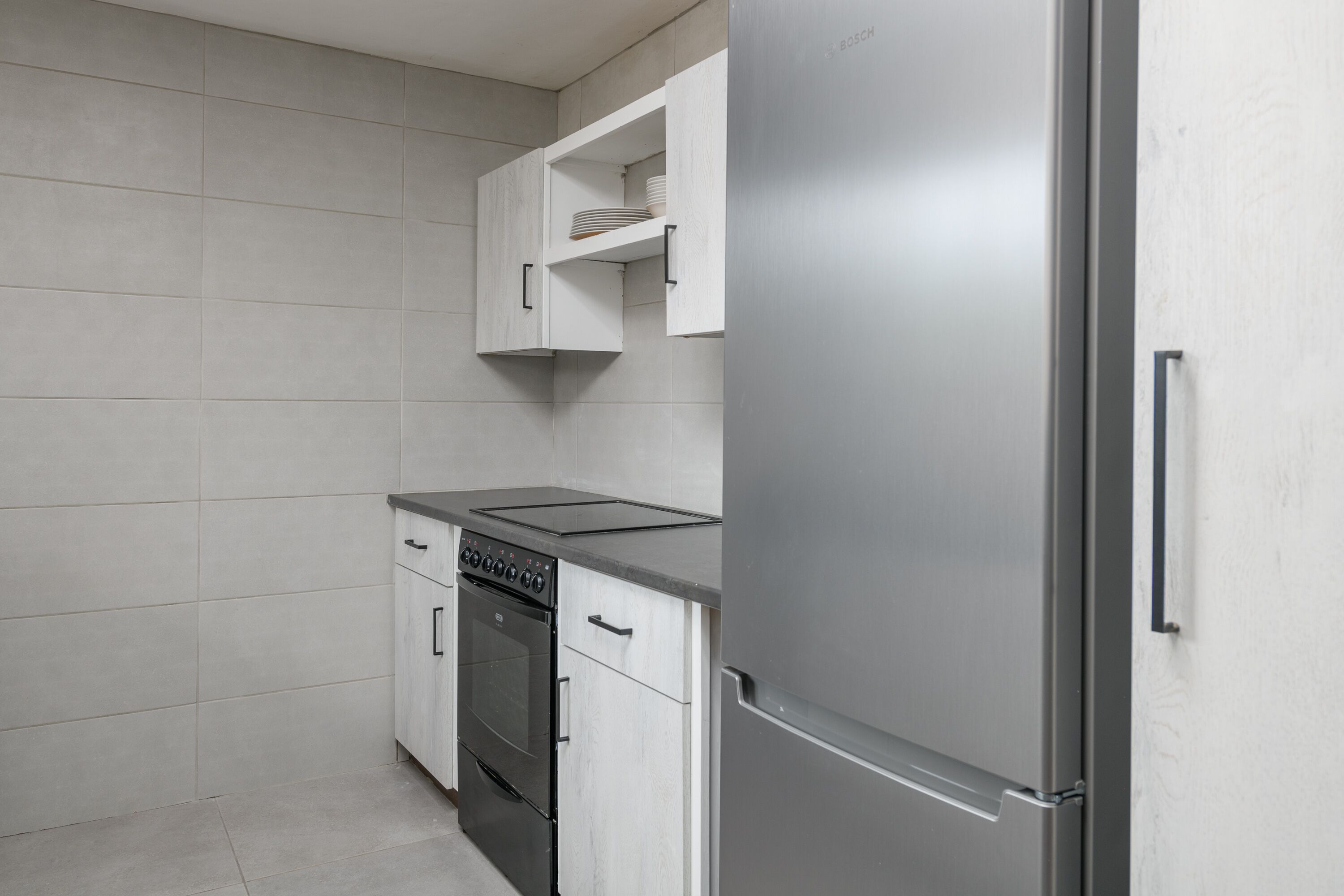 A kitchen with a stainless steel refrigerator, a built-in oven, and white cabinetry.