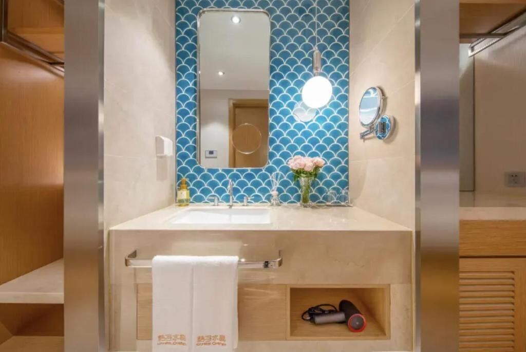 Un baño con pared azul de azulejos, dos lavamanos, un espejo, un perchero y un estante con una toalla y un par de zapatos.