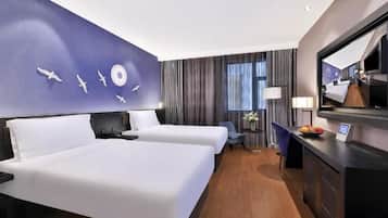 A hotel room with two beds, a desk with a computer, a mirror, and a window with curtains.