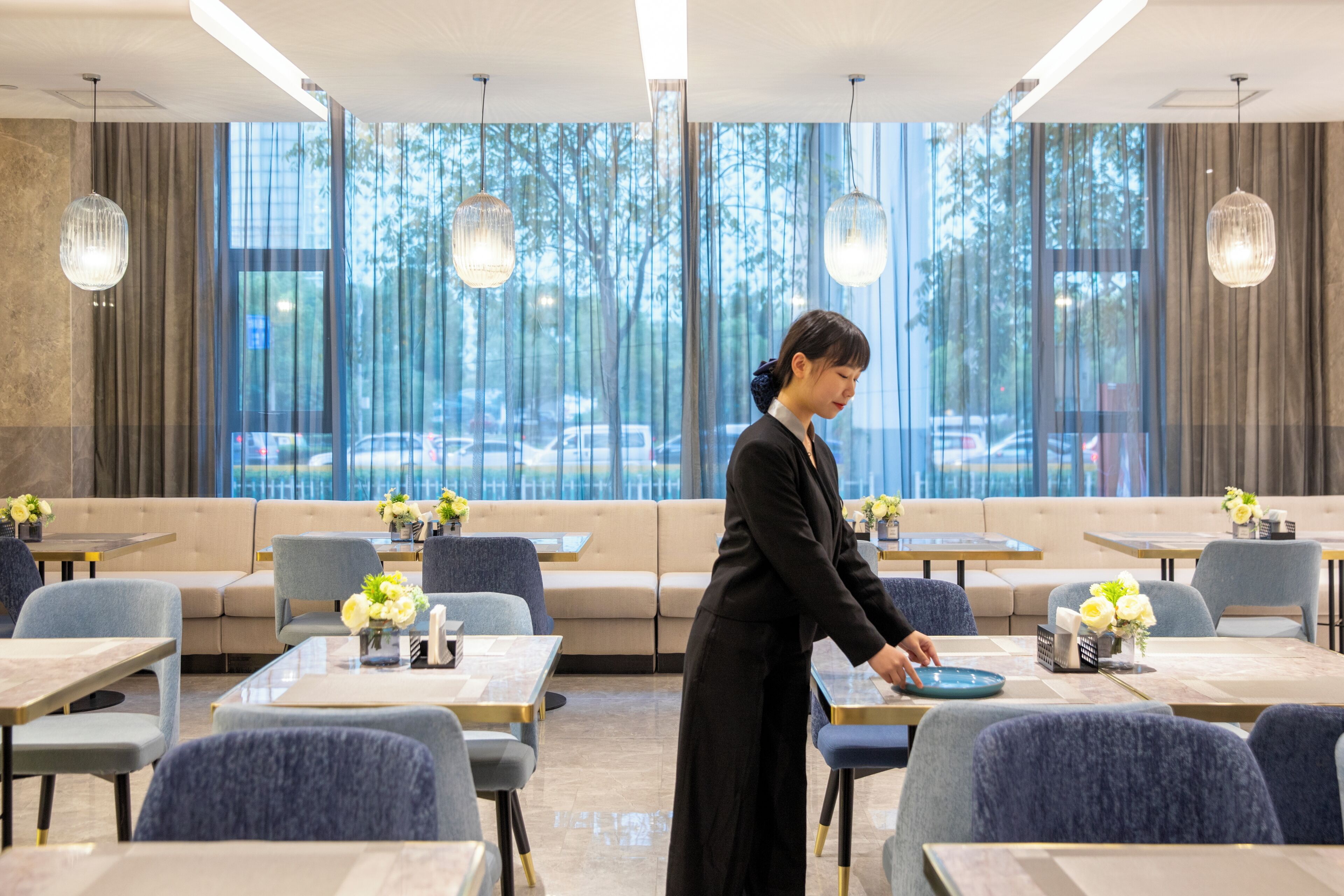 Een restaurantgedeelte in een hotel, met tafels, stoelen en een serveerster.