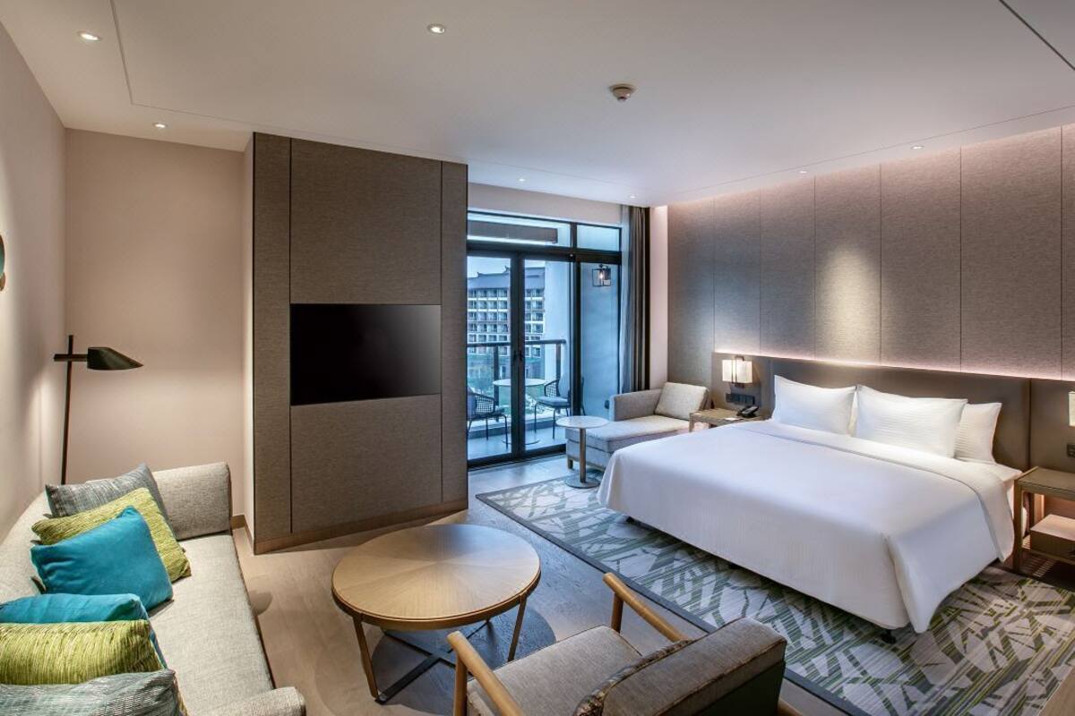 A modern hotel room with a large bed, a sofa, a small round table, and a TV.