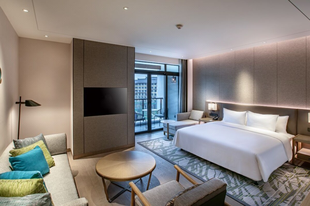 A modern hotel room with a large bed, a sofa, a small round table, and a TV.
