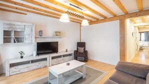 Un salon moderne avec un plafond en bois, un téléviseur à écran plat, un canapé gris et une table basse blanche.