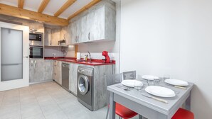 Une cuisine moderne équipée d’un four encastré, d’un four à micro-ondes et d’un lave-linge. On y trouve une table à manger avec des chaises, ainsi qu’une chaise rouge.