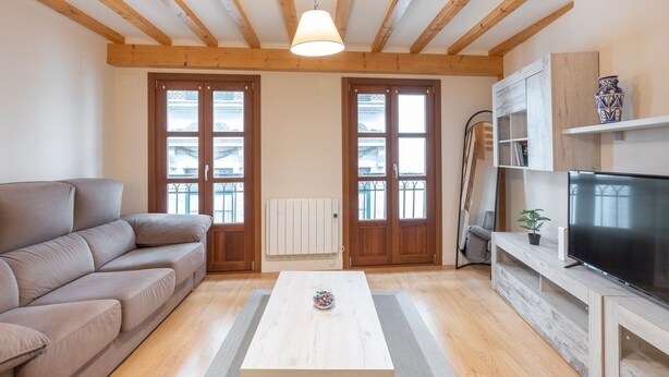 Un salon avec un canapé, une table basse, un téléviseur et des poutres en bois au plafond.