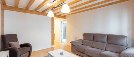 Un salón amplio con techo de madera, un sofá marrón, una mesa de centro blanca y un sillón marrón.