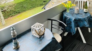 A covered outdoor seating area with a table and chairs, a view of a garden, and a stone wall. - Les Pins Residence: Duplex with a beachfront terrace—just a stone's throw away and in a fantastic location (Carnac)