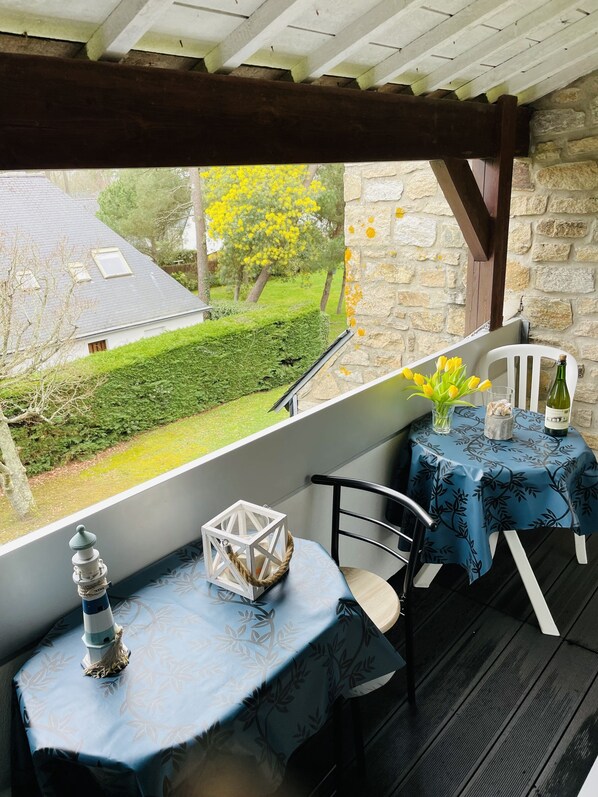 A covered outdoor seating area with a table and chairs, a view of a garden, and a stone wall.