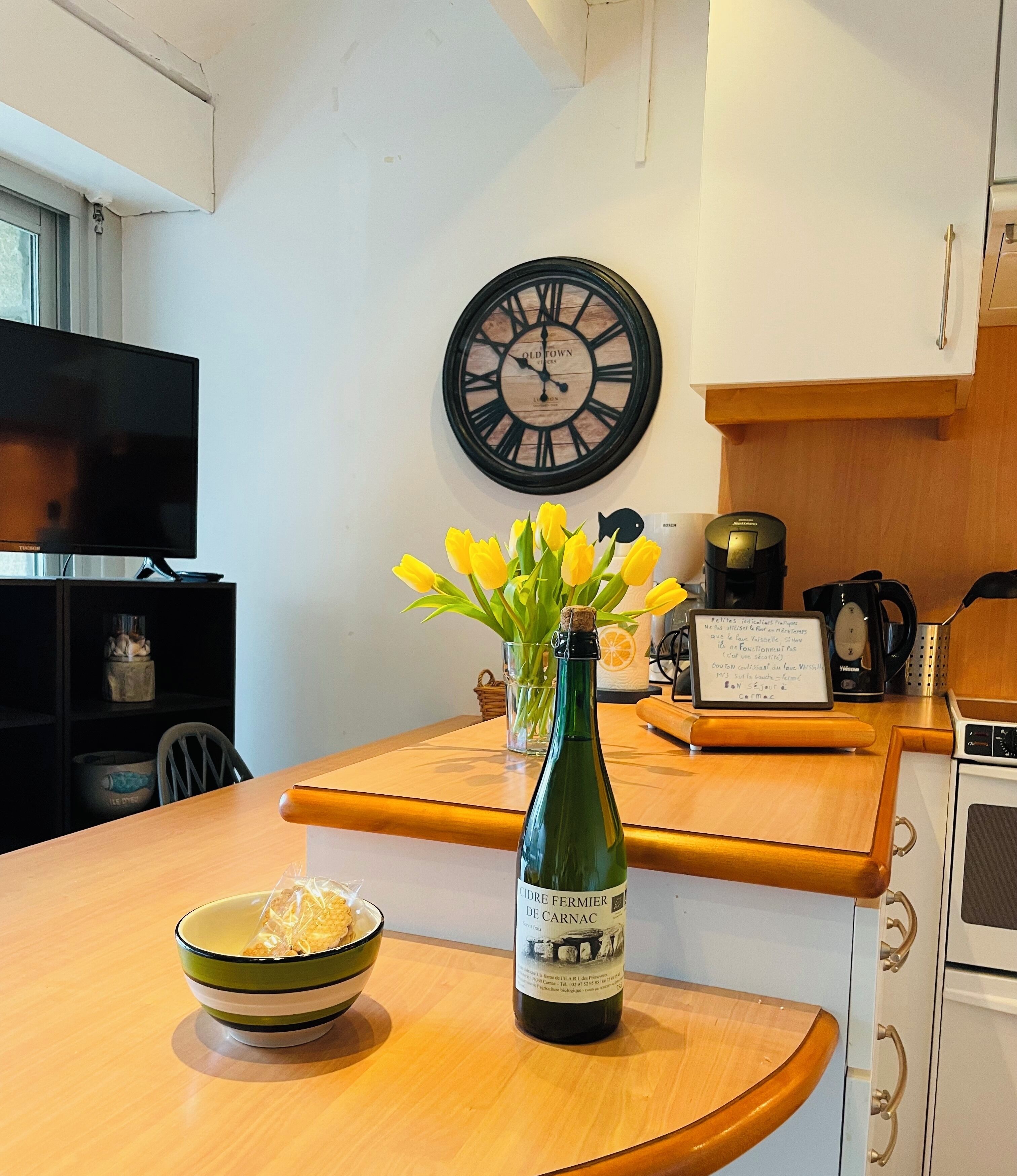 A kitchen with a wooden countertop, a bottle of wine, a bowl, a clock, and a coffee maker.
