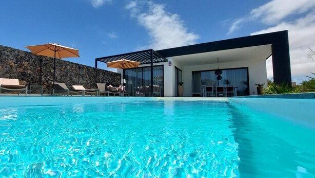 A modern pool area with clear blue water, lounge chairs, and umbrellas. - CASA NIDO - Modern, very spacious villa with heated pool (Lajares)