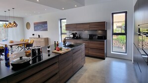 A modern kitchen with a large island, dark wood cabinetry, and a view of the outdoors through a large window. - CASA NIDO - Modern, very spacious villa with heated pool (Lajares)