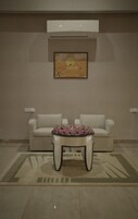 Una sala moderna con un sofá color beige, una mesa de centro de vidrio con flores rosadas y un cuadro en la pared.