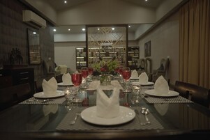 Mesa de comedor preparada para seis personas, con servilletas blancas, copas de vino tinto y un florero con flores.