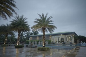 Un edificio moderno con piscina, palmeras y zonas de estar al aire libre.