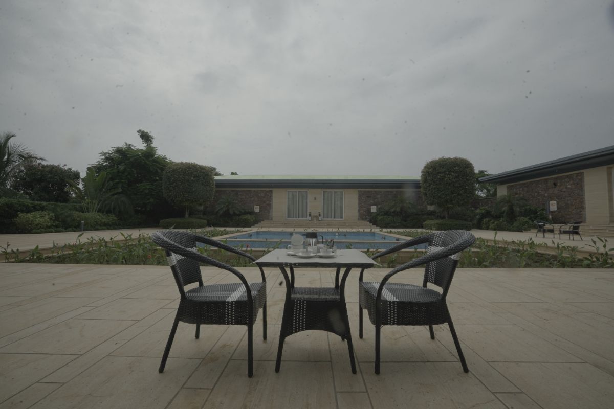 An outdoor patio with a table and chairs, a swimming pool in the background, and a building with a green roof.