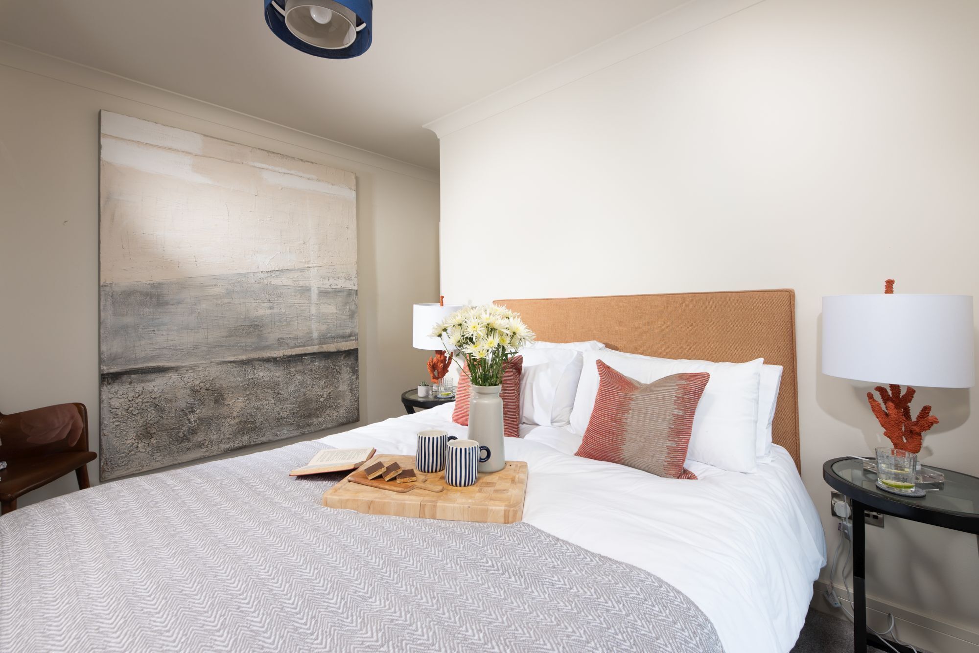 Habitación de hotel ordenada con una cama grande, una mesita de noche de madera, una mesita redonda pequeña y una lámpara de pared.
