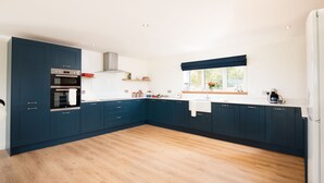 A modern kitchen with dark blue cabinets, a built-in oven, and a window with a view of greenery. - WESTWOOD COTTAGE - A spacious farm cottage close to superb East Lothian beaches  (Longniddry)
