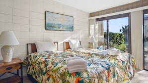 Ein Hotelzimmer mit einem großen Bett, zwei Nachttischen, einem Bild an der Wand und Blick ins Freie durch eine Schiebetür.