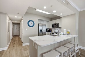 A modern kitchen with a central island, stainless steel appliances, and a clock on the wall.