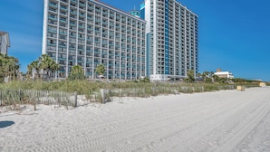 A high-rise hotel with multiple balconies, located adjacent to a sandy beach.